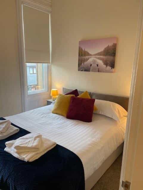 Bedroom with white linens, colorful pillows, and a landscape painting above the bed
