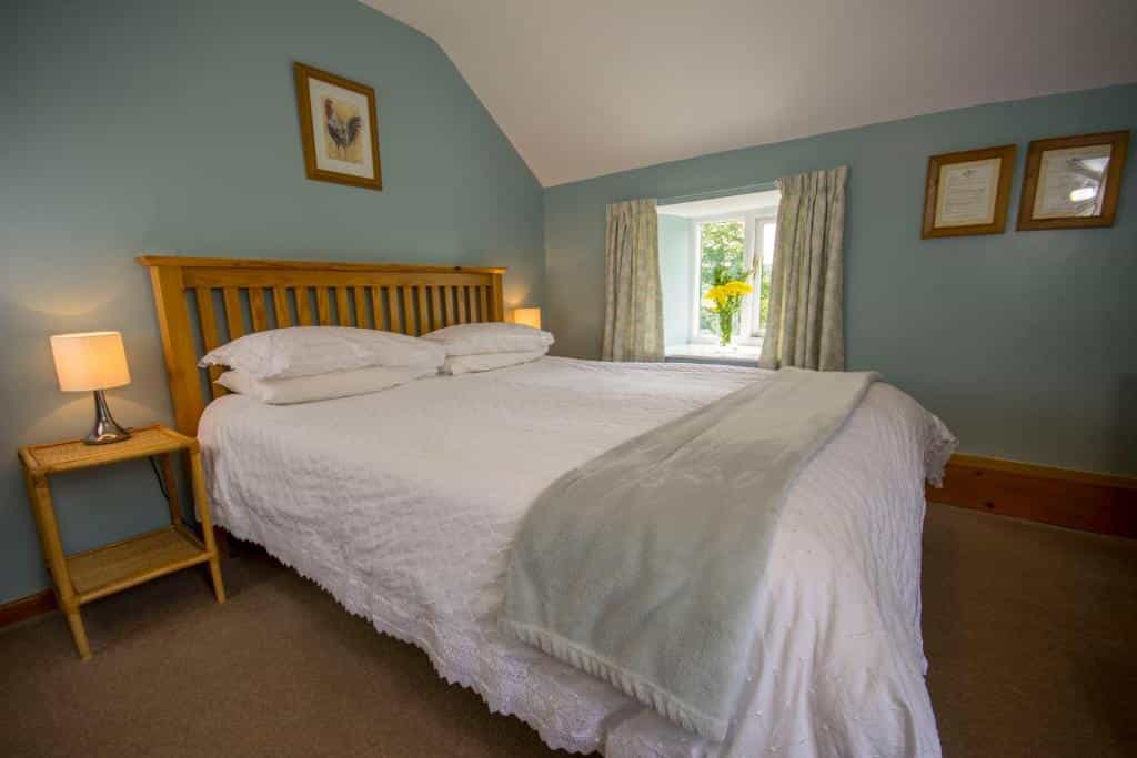 Bedroom with wooden headboard, white bedding, and light blue walls, window with yellow flowers.