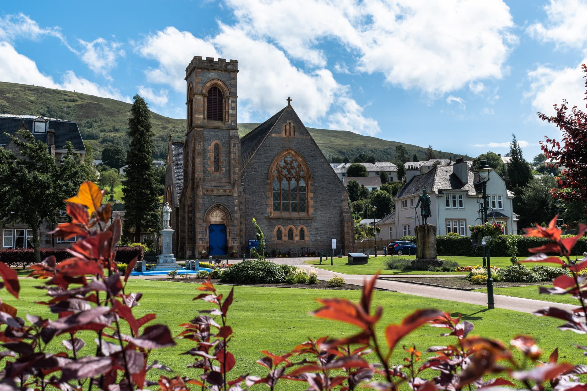 Stone church with tower and blue door, green lawn, and hills in Duncansburg-Fort William.