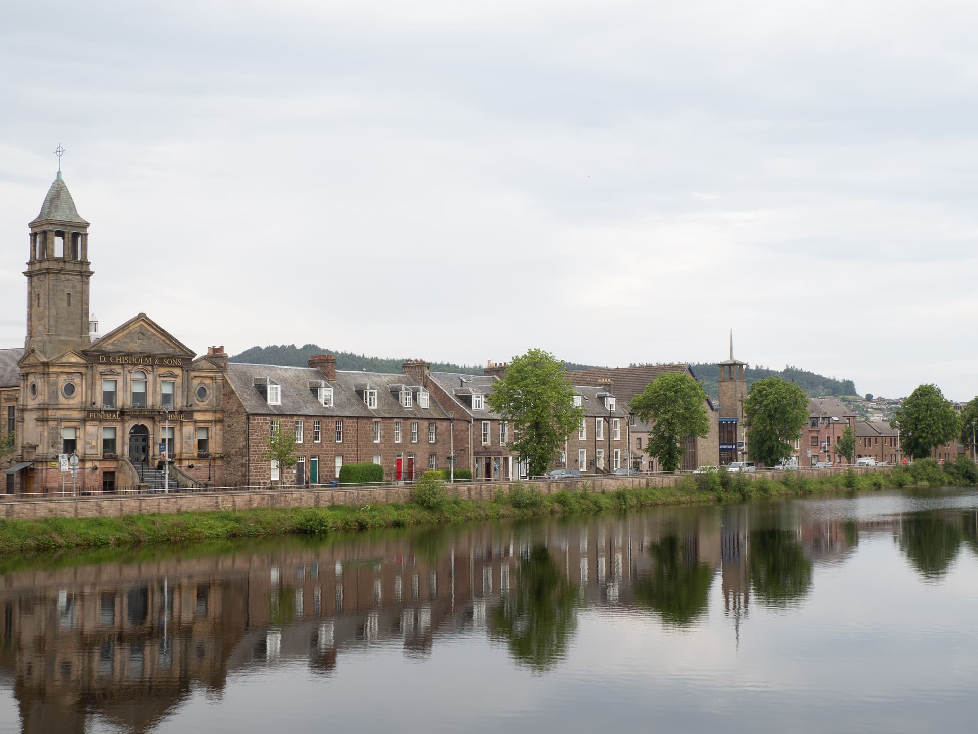 Riverside buildings and a stone tower reflected in the water in Skyline de Inverness.