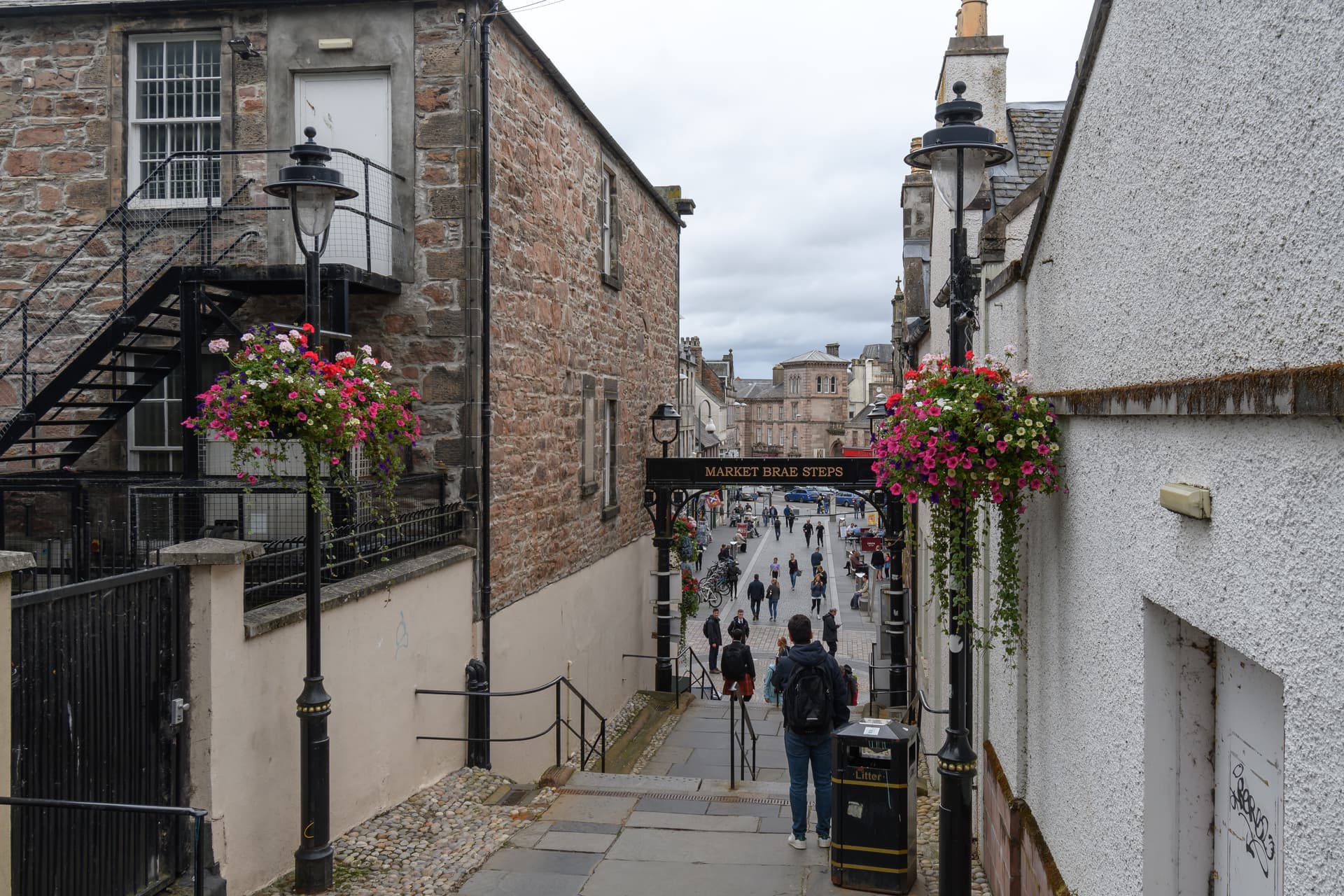 View down Market Brae Steps in Inverness toward a busy street with pedestrians and stone buildings.
