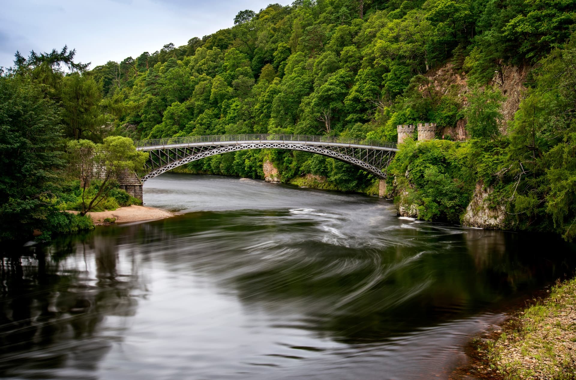 Iron bridge over the River Spey with motion blur on dark water and lush green banks.