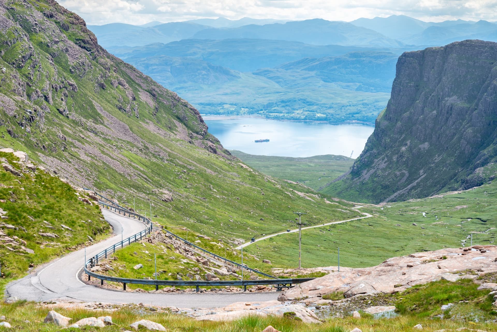 Winding mountain road descending into a valley overlooking a loch at Bealach na Bà pass.