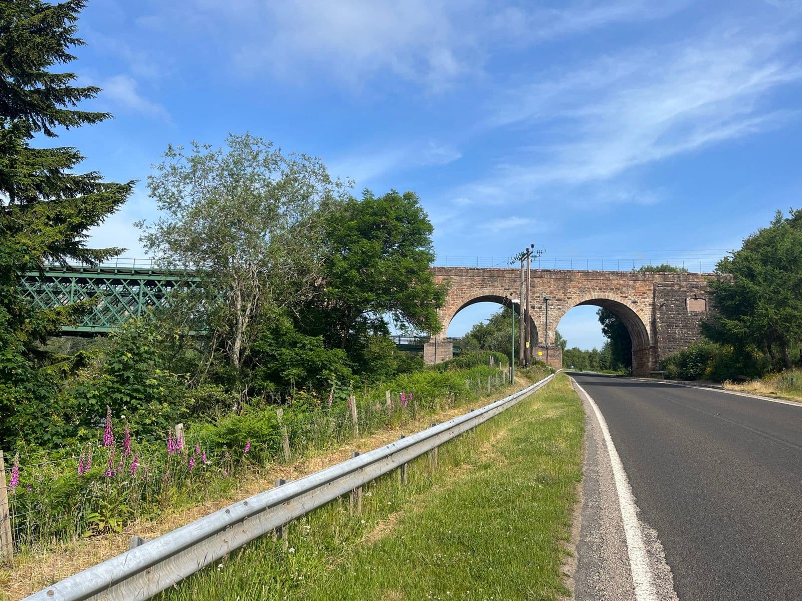 Road passing under a stone arch bridge and a green metal railway bridge near Inverness.