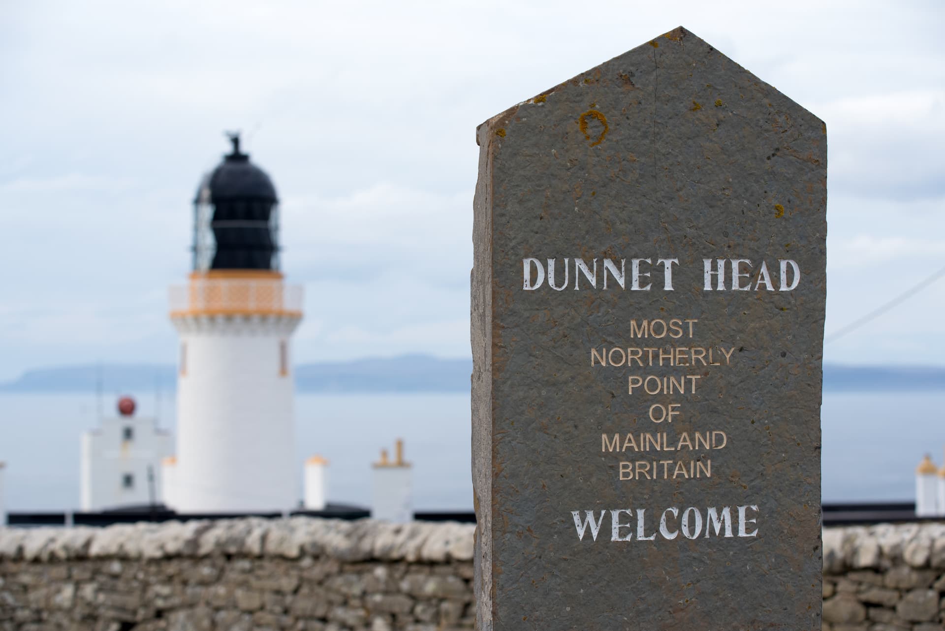 Dunnet Head welcome sign with lighthouse in background over the sea.