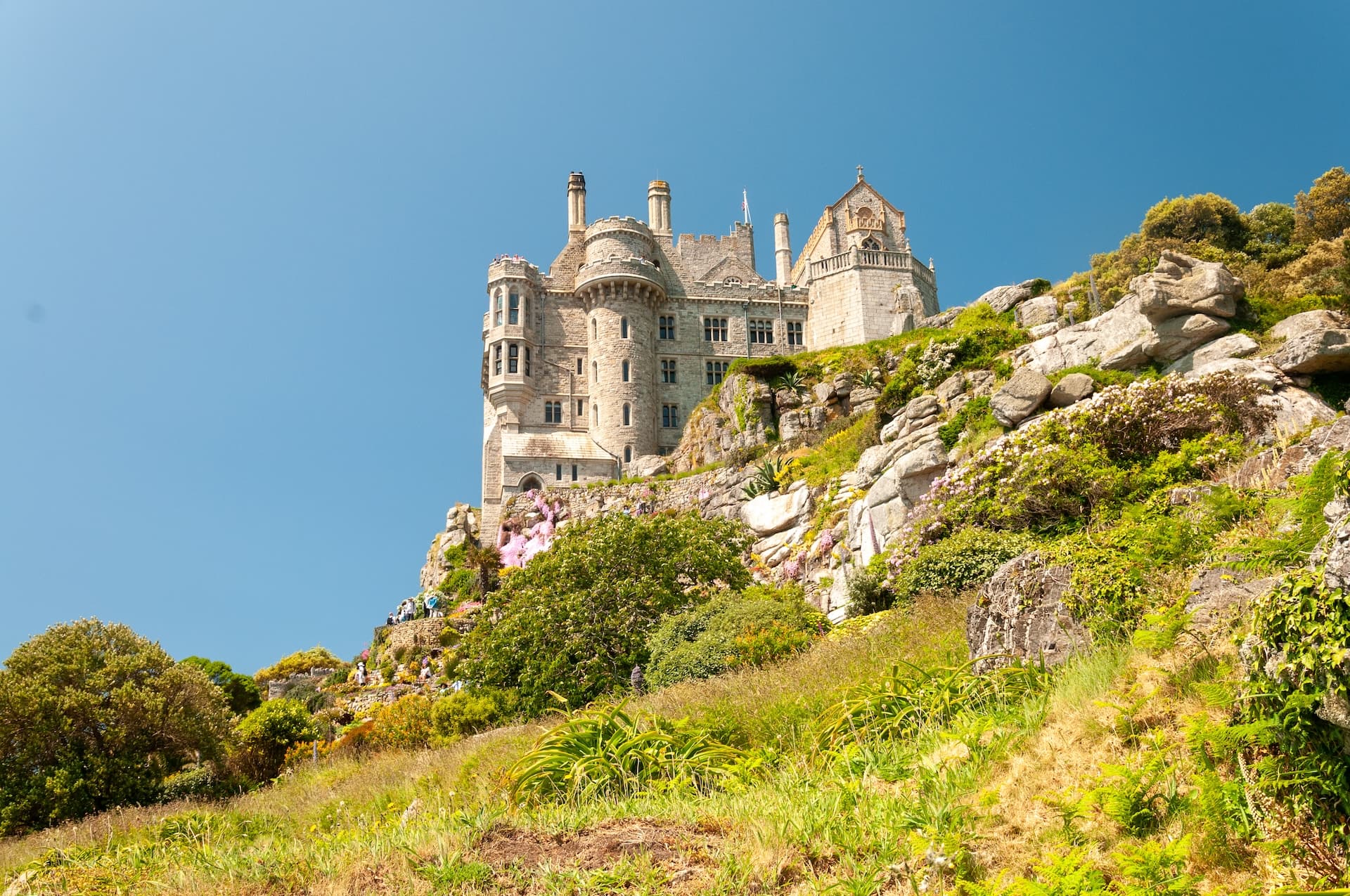 St Michael's Mount castle perched on rocky hillside with lush green vegetation under clear blue sky.