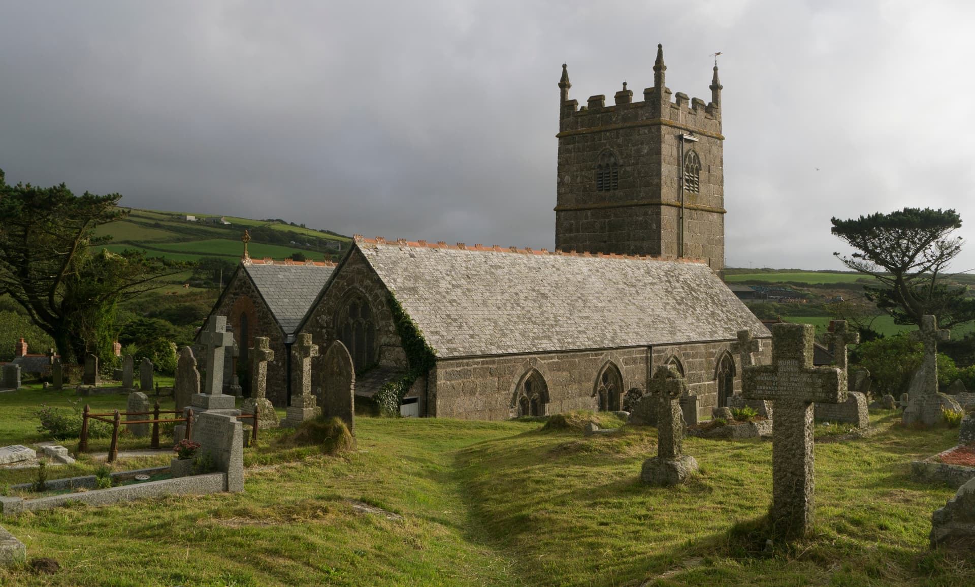 Stone church with tower and ancient gravestones in a grassy churchyard near green hills.
