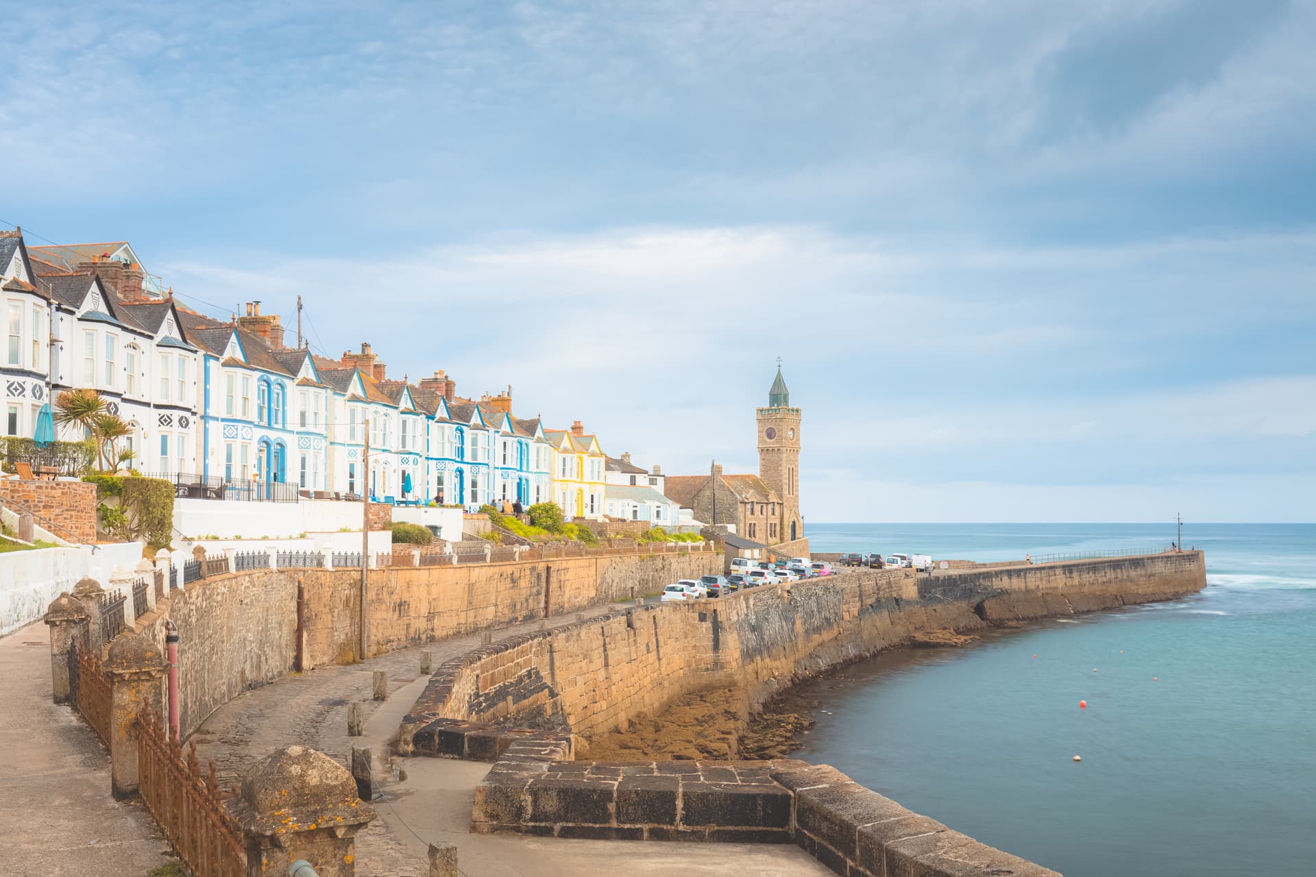 Porthleven harbor with colorful seaside terrace houses and a stone clock tower by the sea.
