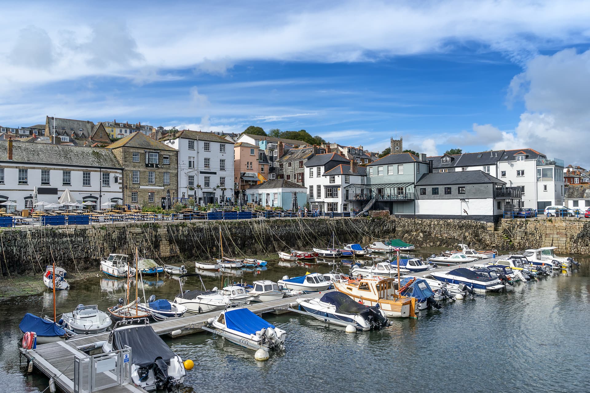 Boats moored in harbor with historic waterfront buildings and blue sky in Falmouth.