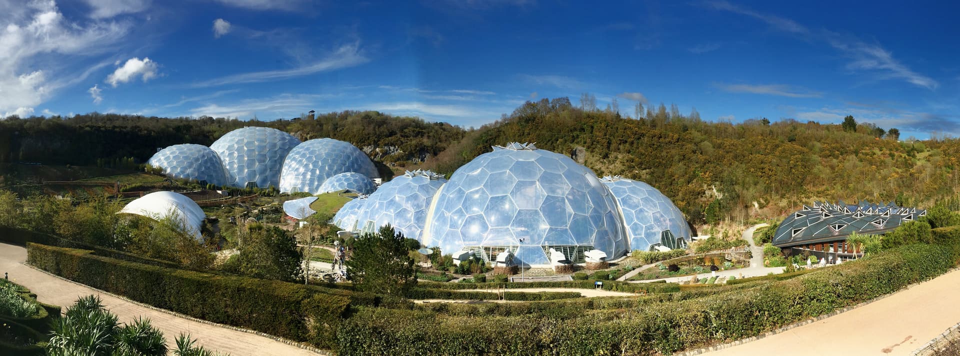 Geodesic domes of the Eden Project surrounded by green hills under a bright blue sky.