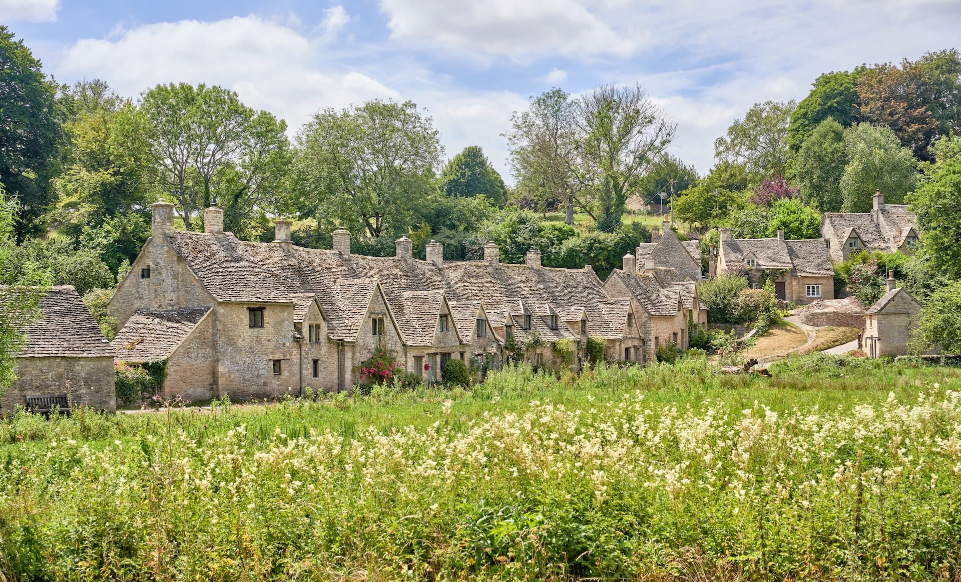 Stone cottages with slate roofs behind a field of tall white wildflowers in Bibury.