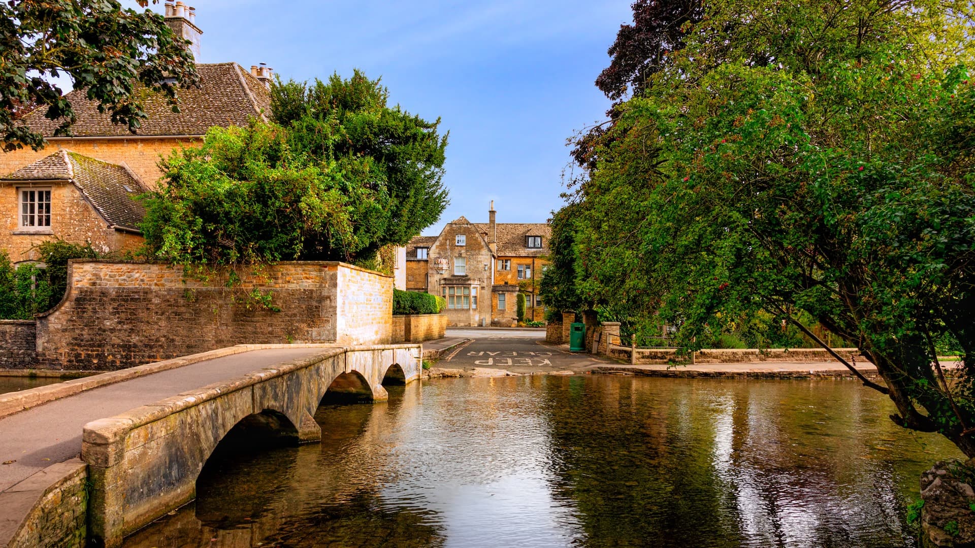 Stone arched bridge over water in Bourton-on-the-Water with Cotswold stone buildings.