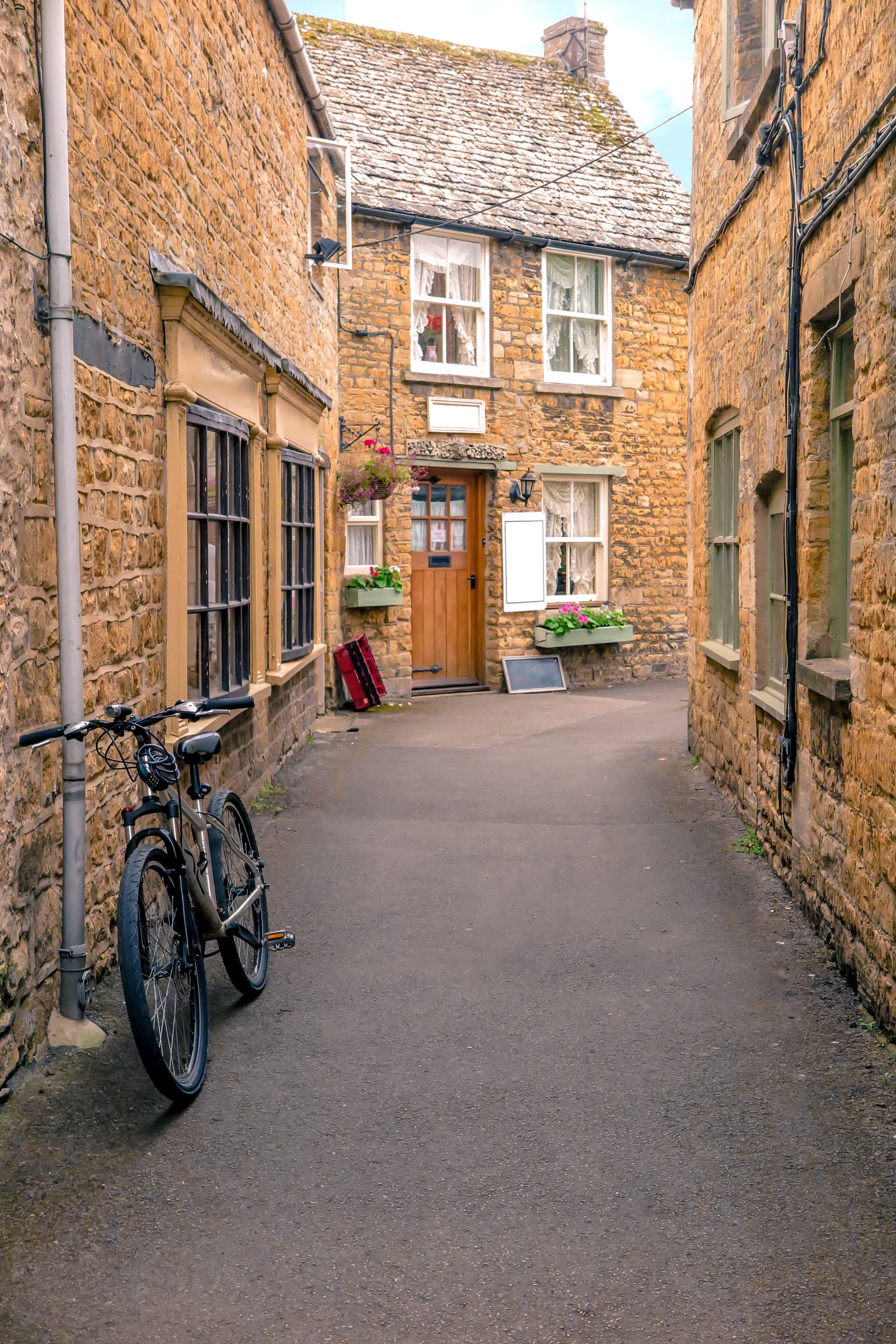 Bicycle parked on narrow lane between stone buildings in Bourton