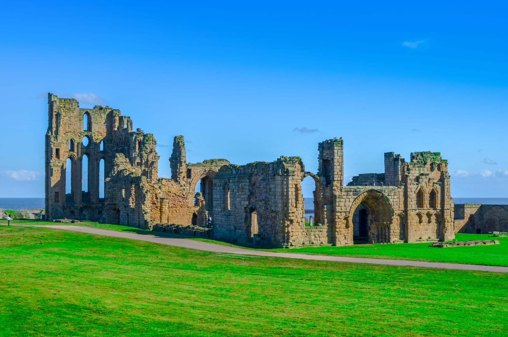 Stone abbey ruins on green grass overlooking the sea under a bright blue sky
