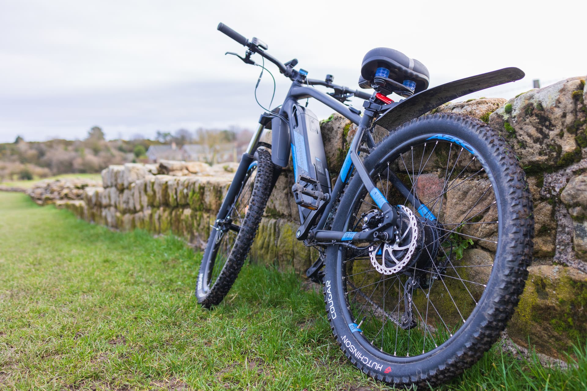 Electric bike leaning against a mossy stone wall on grass, near Hadrian's Wall.
