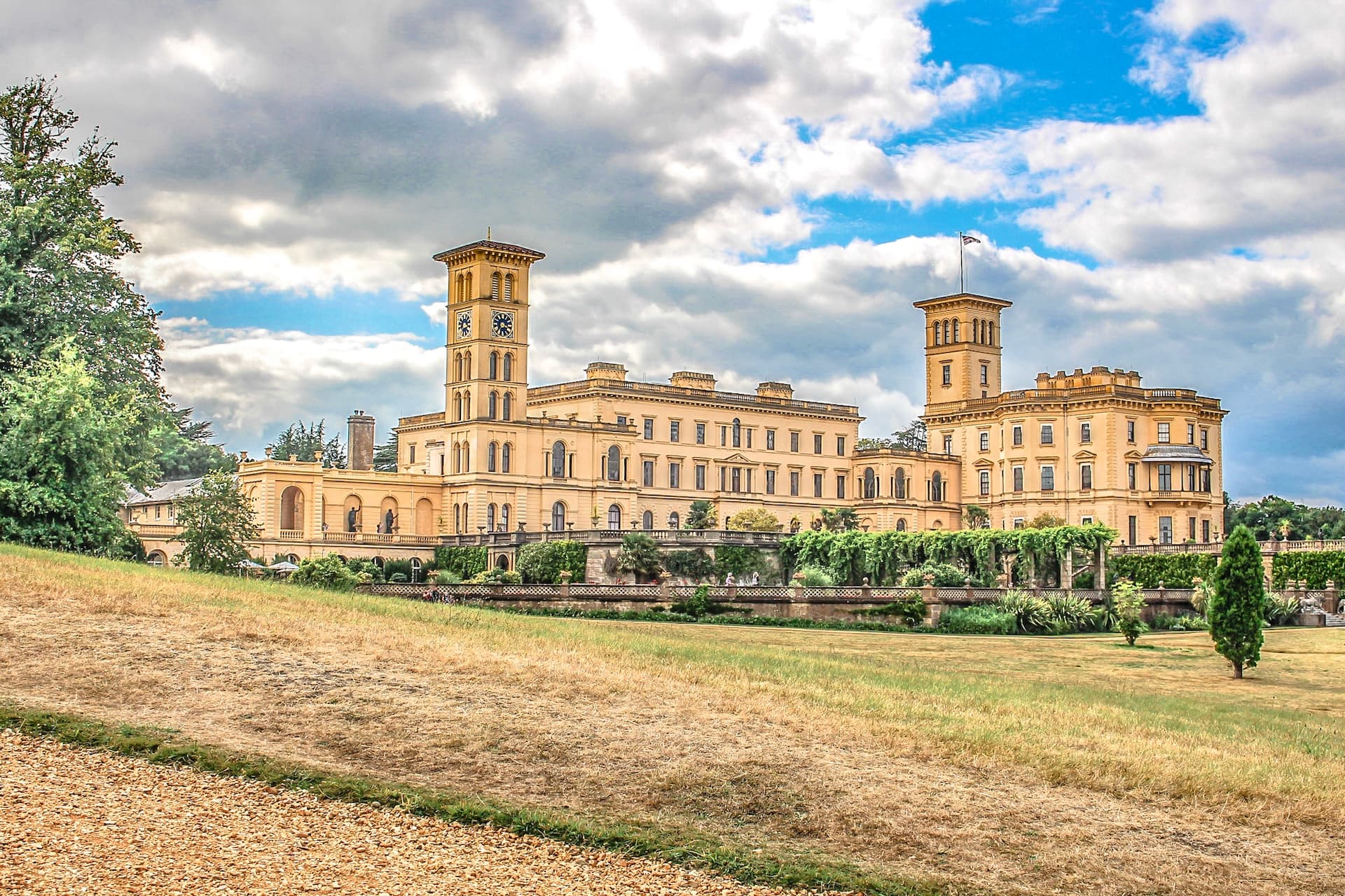 Osborne House with clock towers and gardens under a dramatic cloudy blue sky