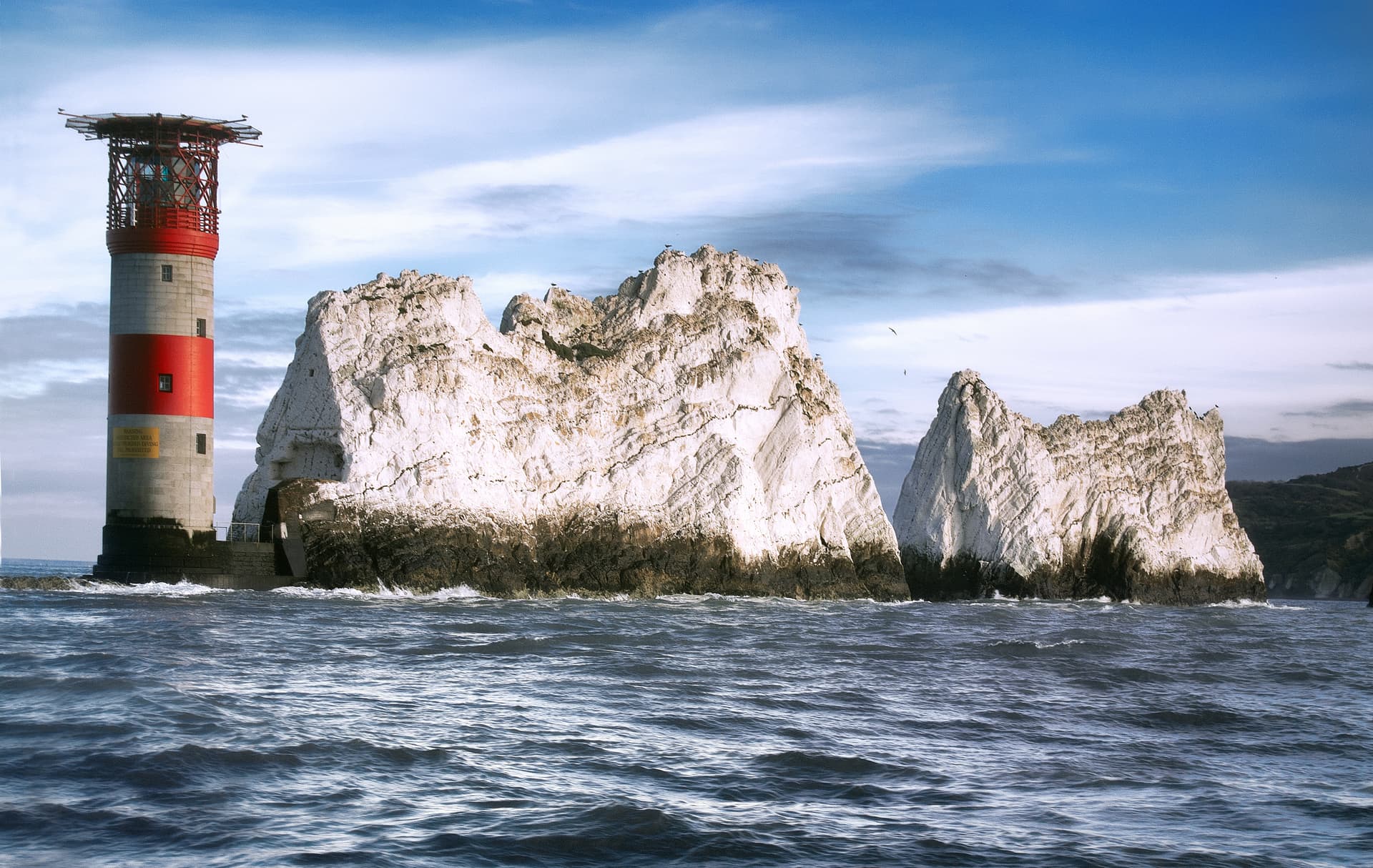 Lighthouse next to white chalk sea stacks with choppy water and blue sky, The Needles.