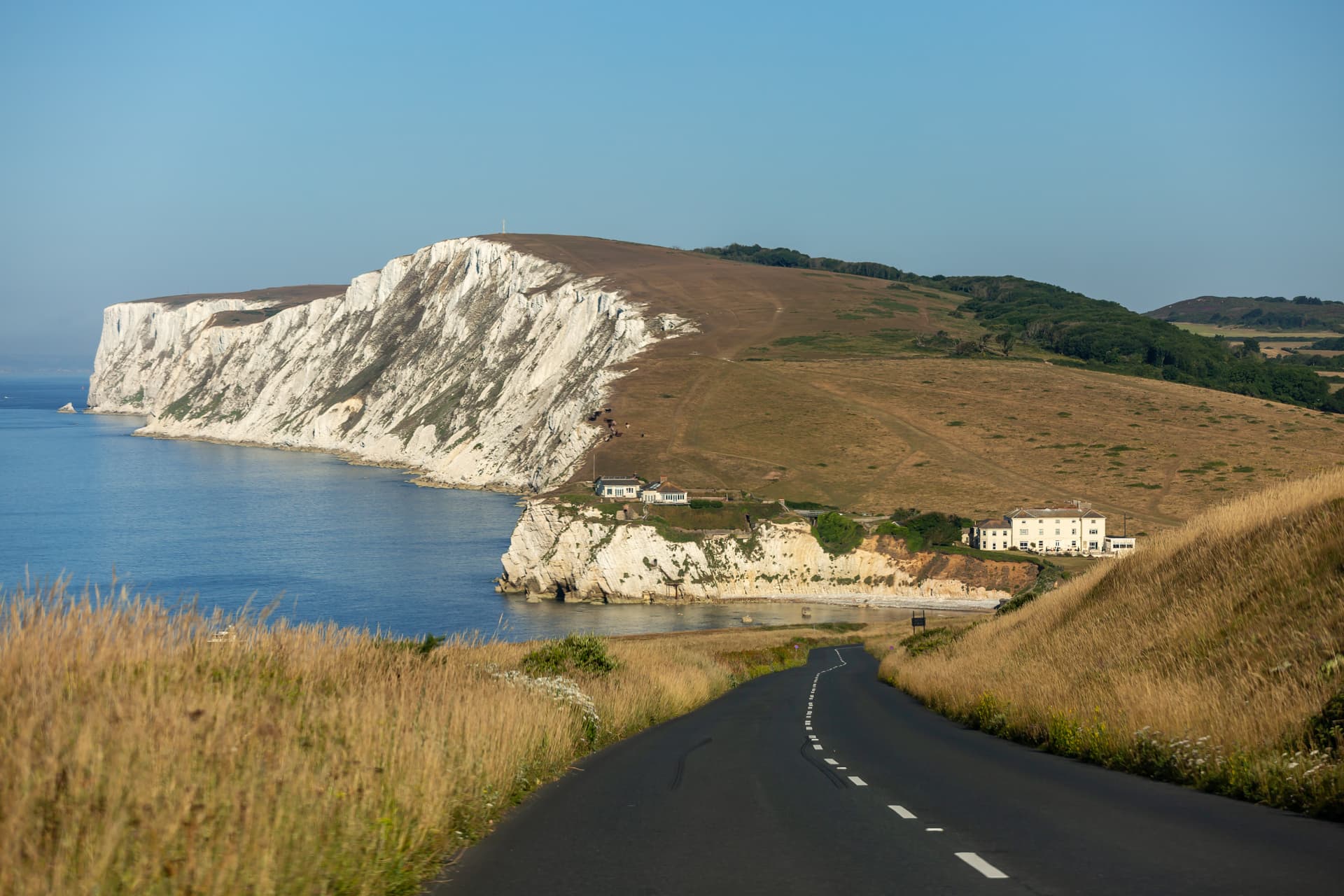 Winding road past white chalk cliffs and buildings overlooking blue sea water