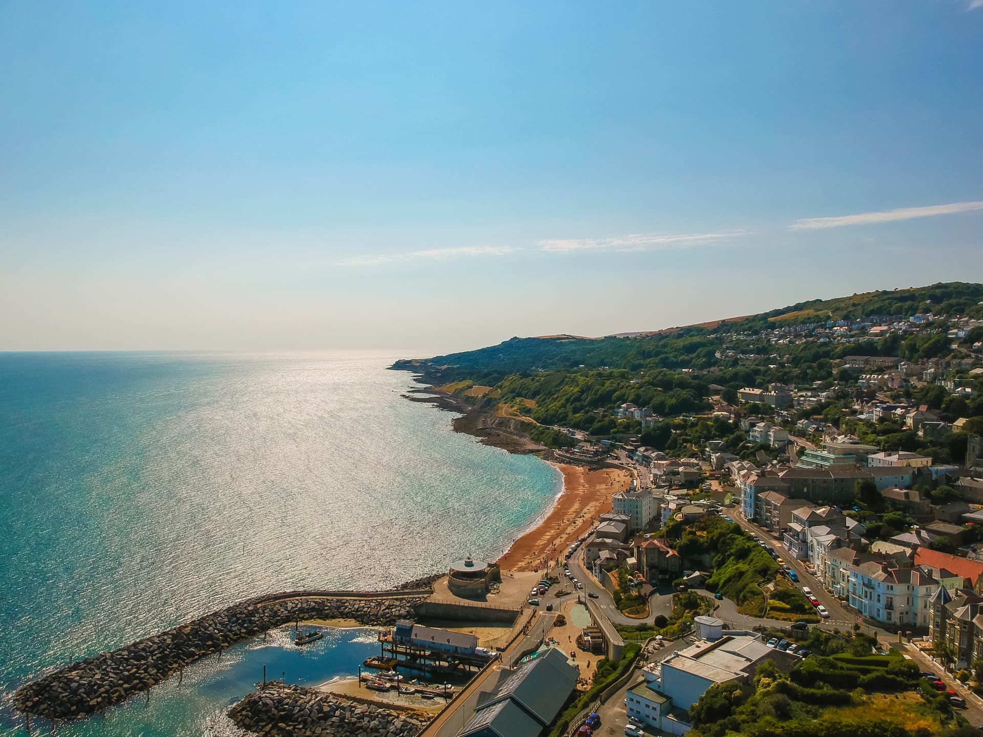 Aerial view of Ventnor coastal town with harbor, beach, and steep green hills under a clear blue sky.