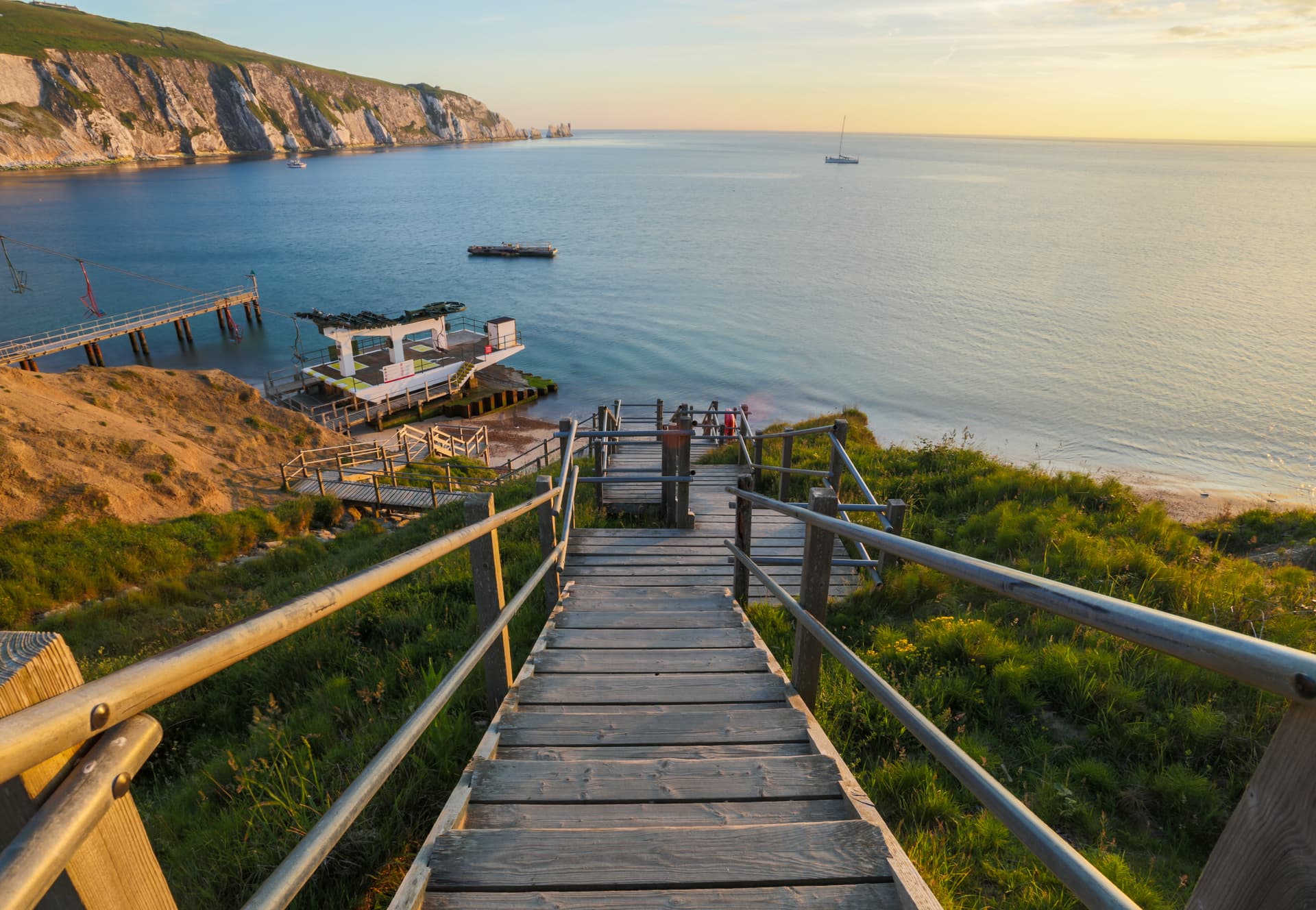 Wooden steps down to coast with chalk cliffs and sailboat at sunset