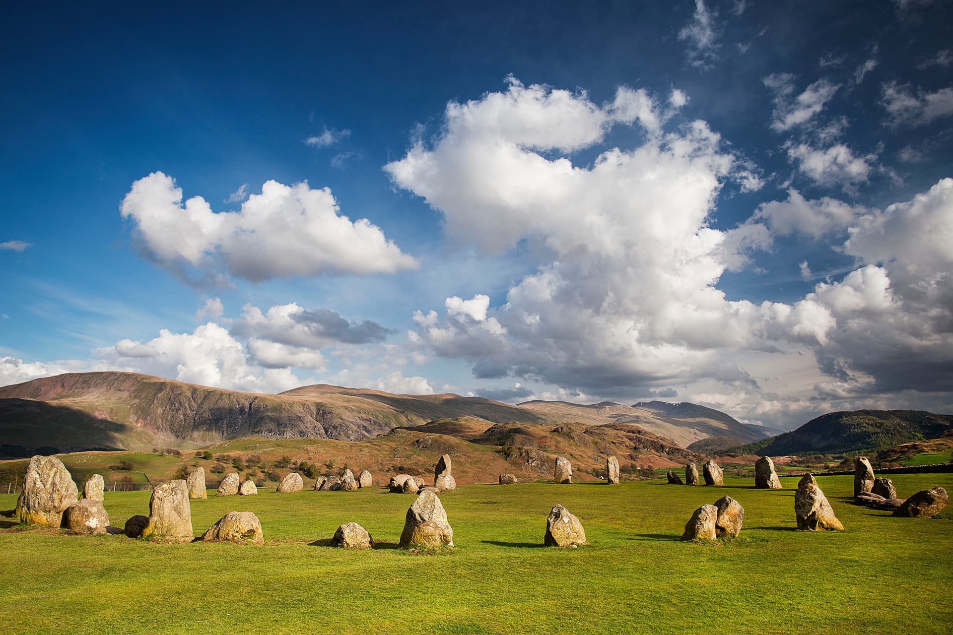 Castlerigg Stone Circle on green grass with rolling hills and dramatic clouds in the background.