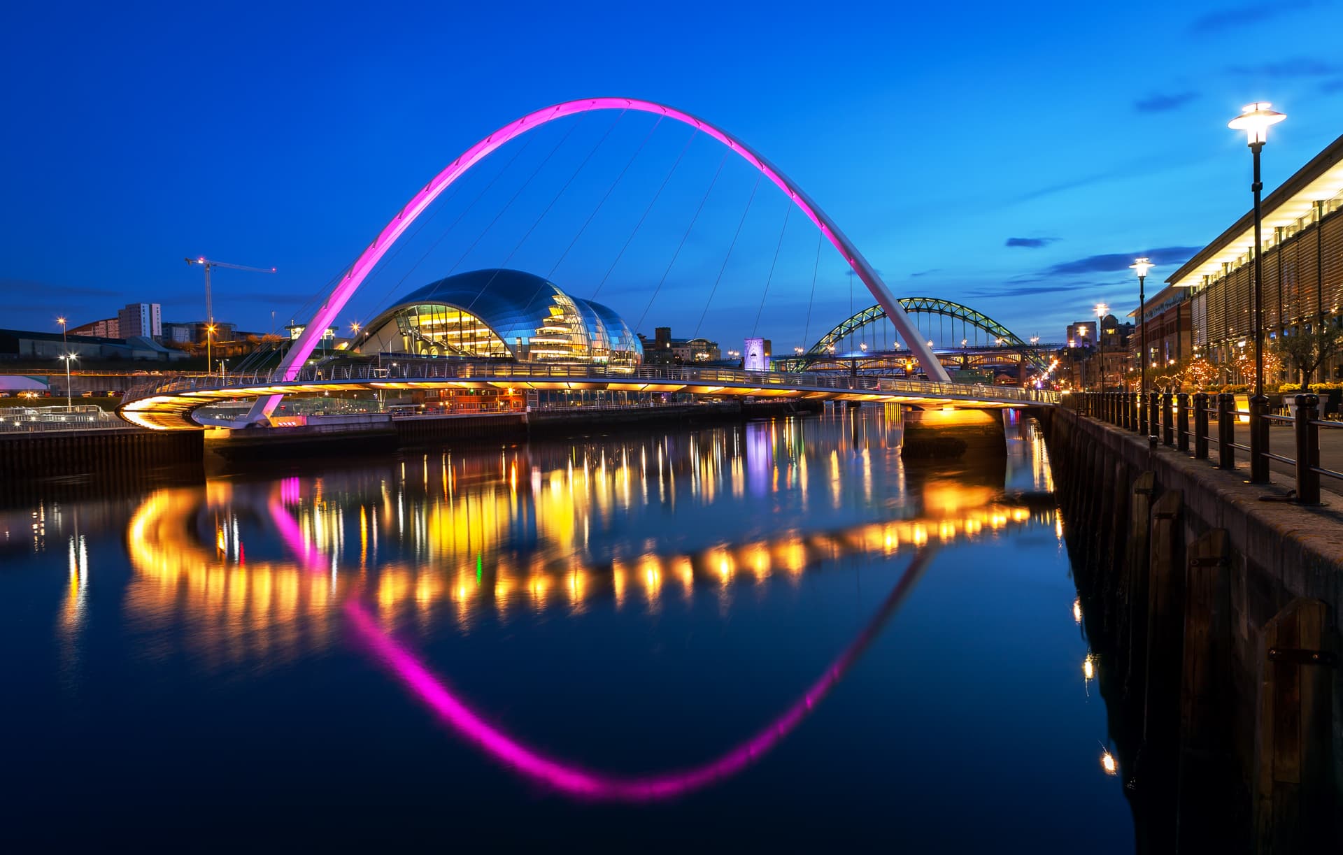 Gateshead Millennium Bridge illuminated pink over river at twilight with reflections.