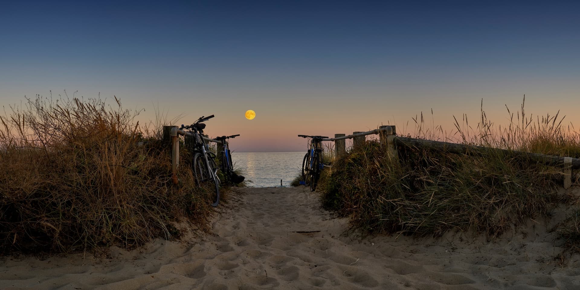 Cycling path to the sea at twilight with bicycles and a bright moon over the water, Tynemouth.