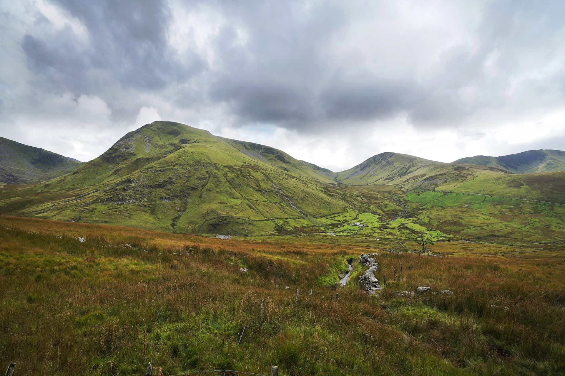 Green rolling mountains under a dramatic cloudy sky in Snowdonia with foreground moorland.