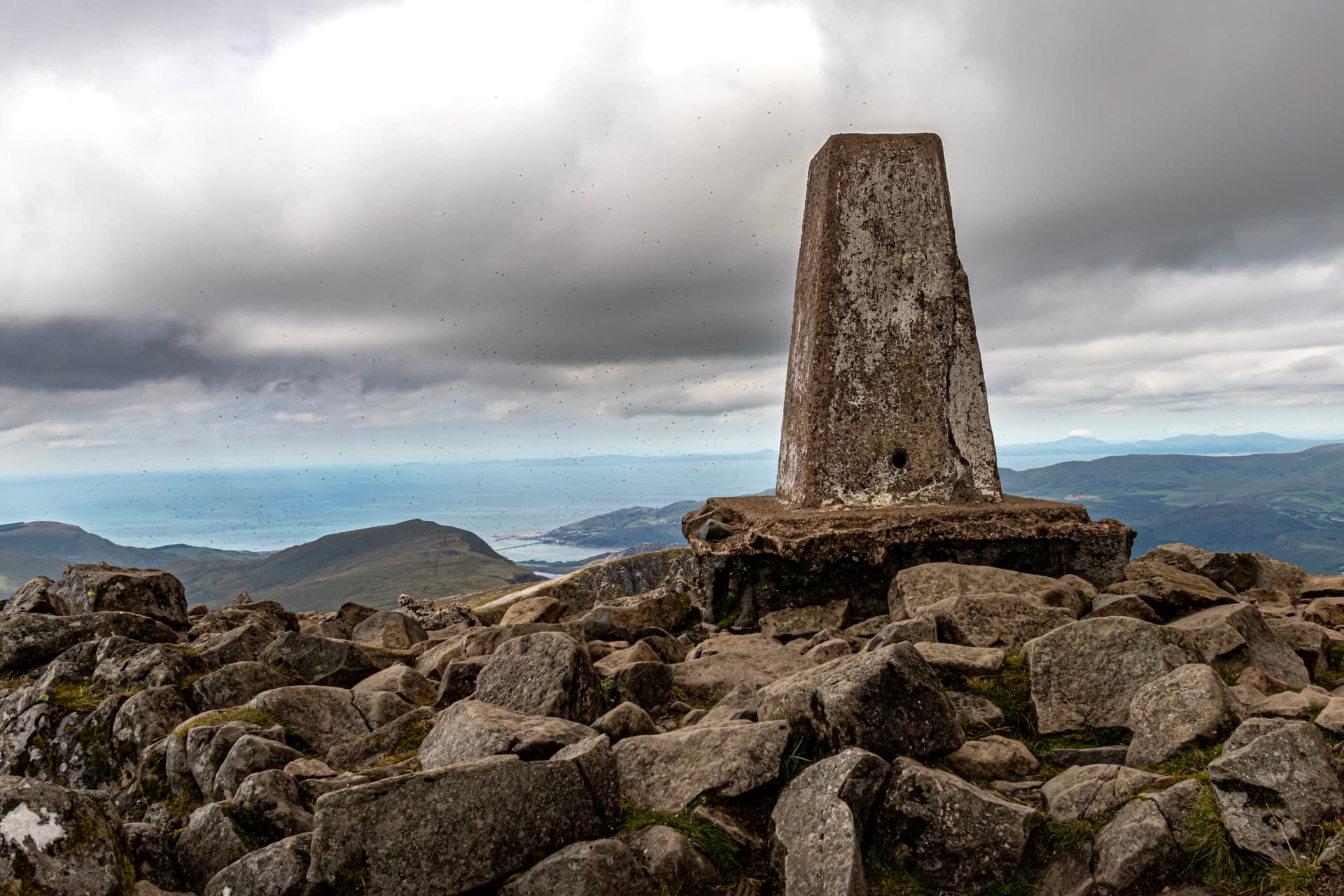 Trig pillar on rocky summit overlooking sea and green mountains, Cadair Idris.