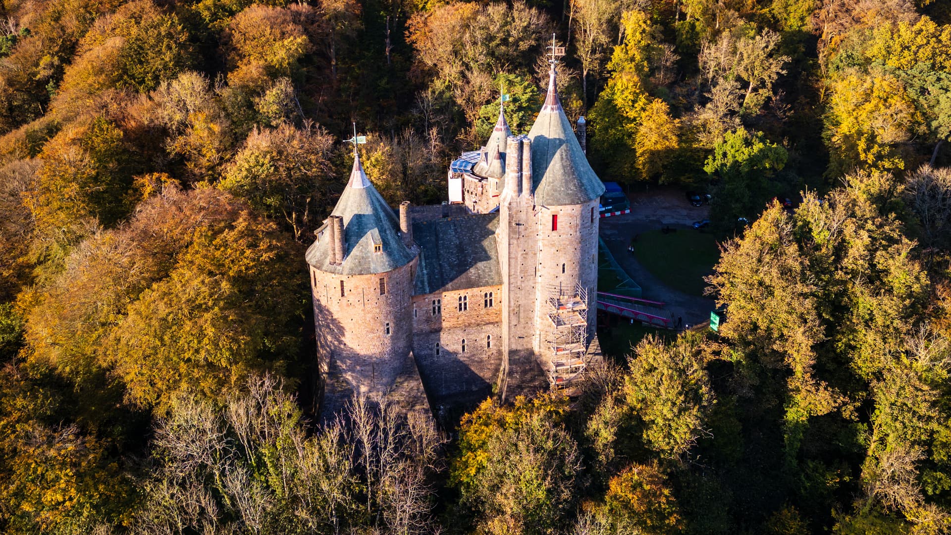 Castell Coch castle surrounded by dense forest with autumn foliage, aerial view.