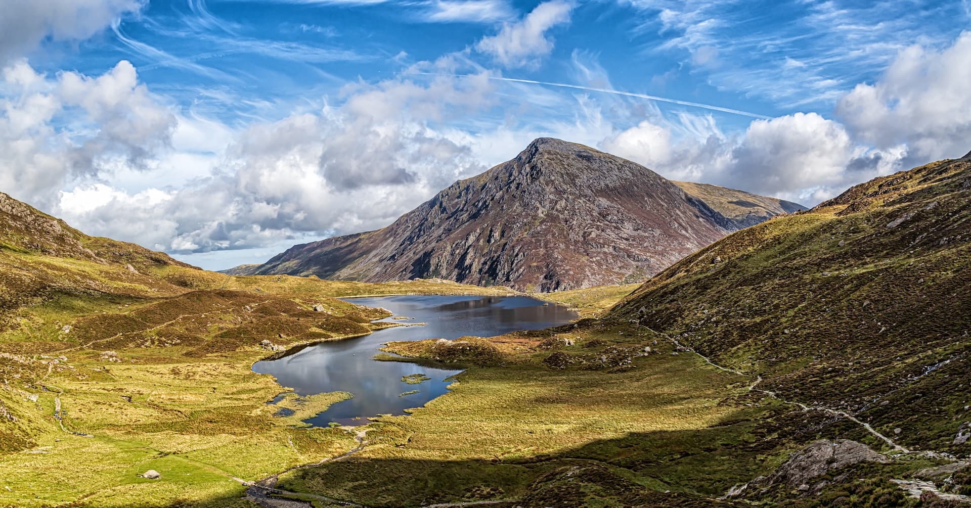 Mountain lake surrounded by rugged hills under a dramatic cloudy blue sky, Snowdonia.