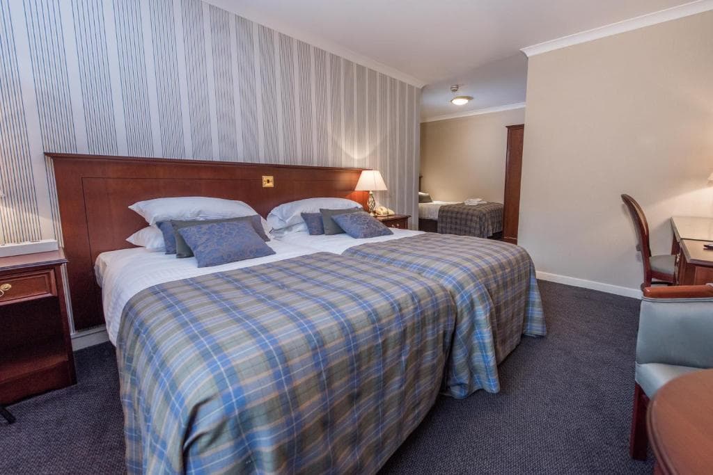 Twin beds with blue plaid blankets in a hotel room, view into an adjoining room.