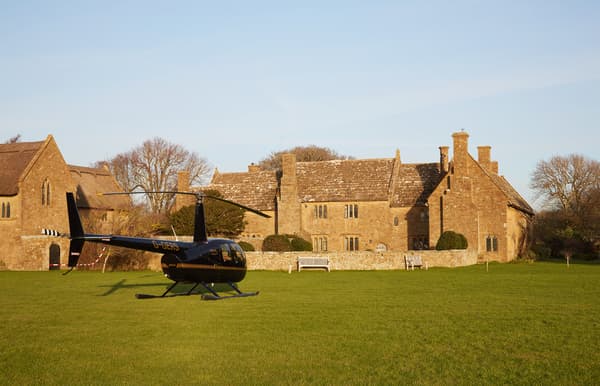 Black helicopter parked on a green lawn in front of a historic stone manor house.