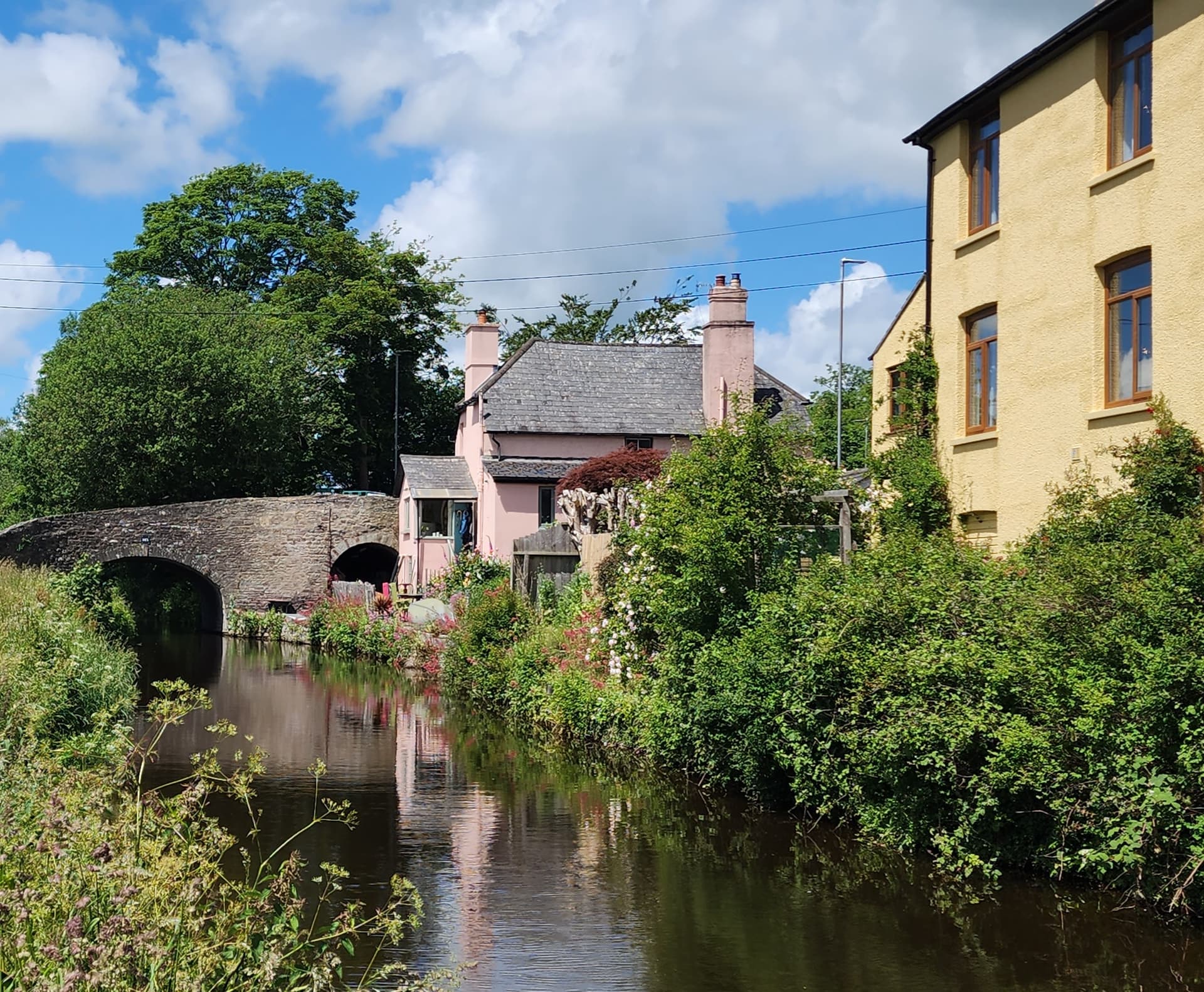 Old stone bridge over a canal with houses and lush greenery