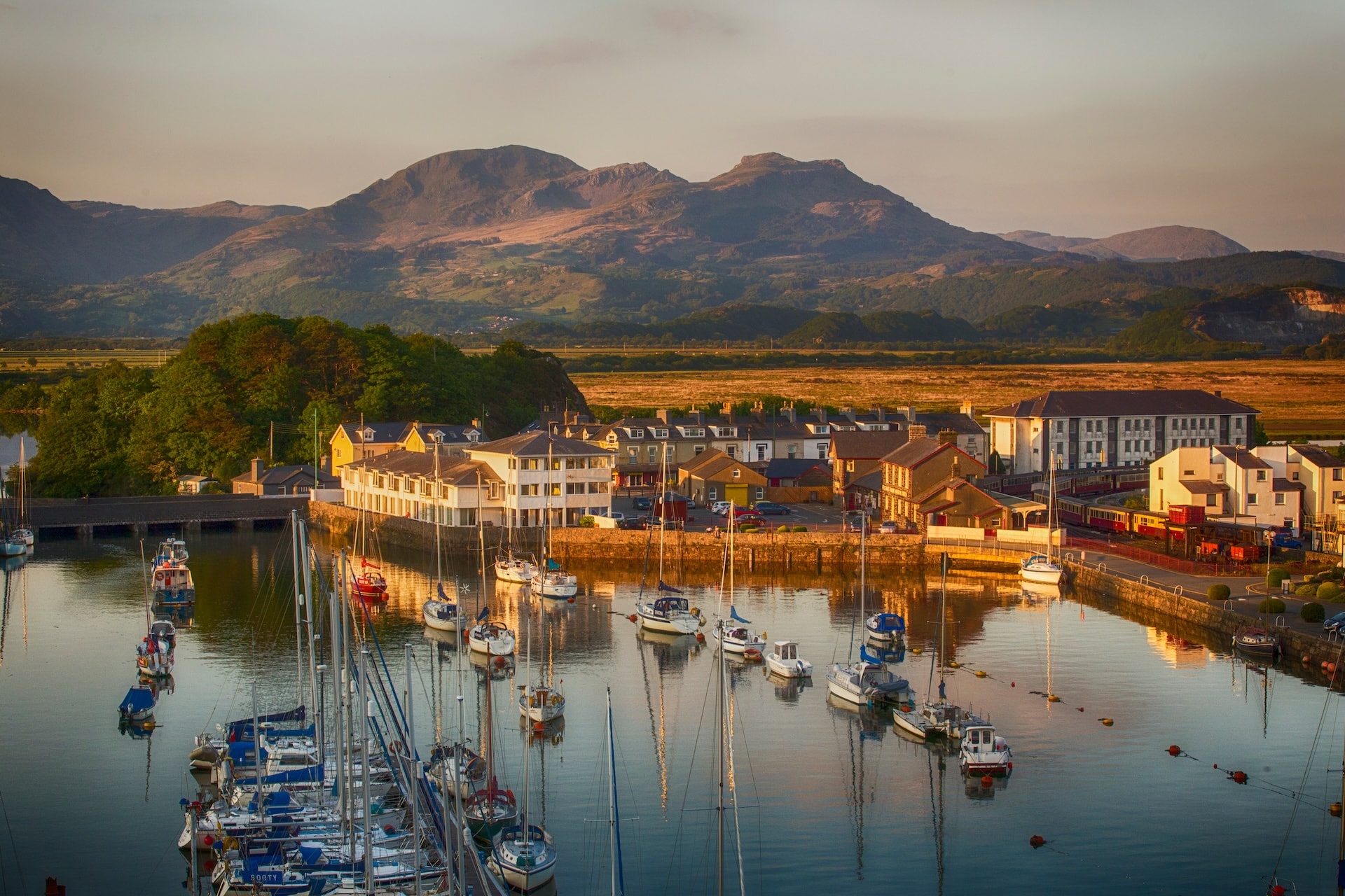 Sailboats moored in the harbor of Porthmadog with mountains in the background at sunset.