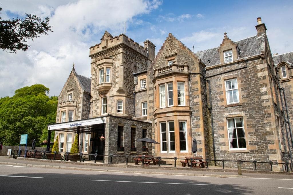 Stone Tarbet Hotel building with outdoor seating area beside a road under a blue sky.