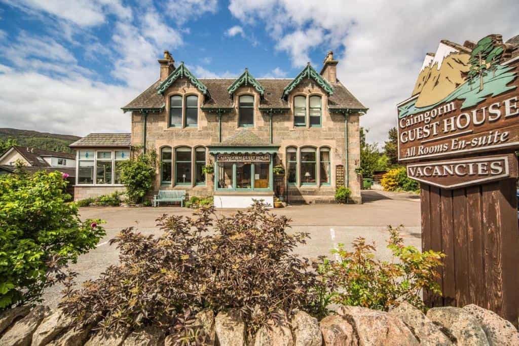 Cairngorm Guest House stone building with Vacancies sign and mountain backdrop.