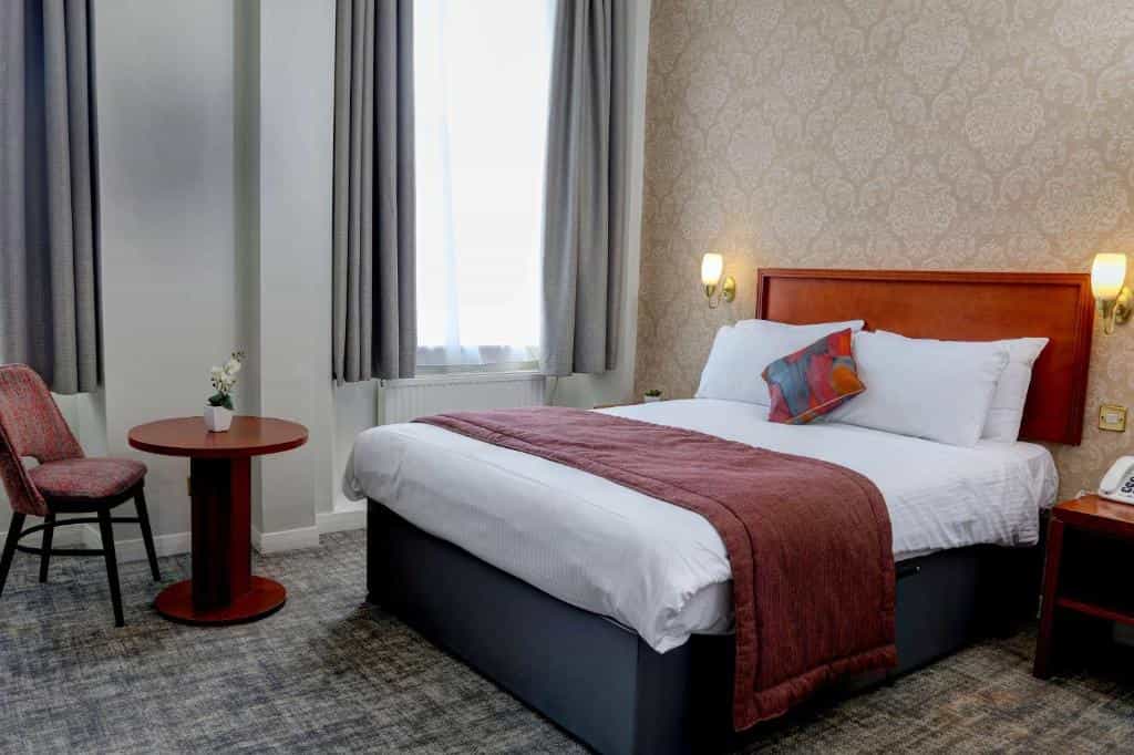 Best Western Queens Hotel room with white bedding, wood headboard, and patterned wallpaper.