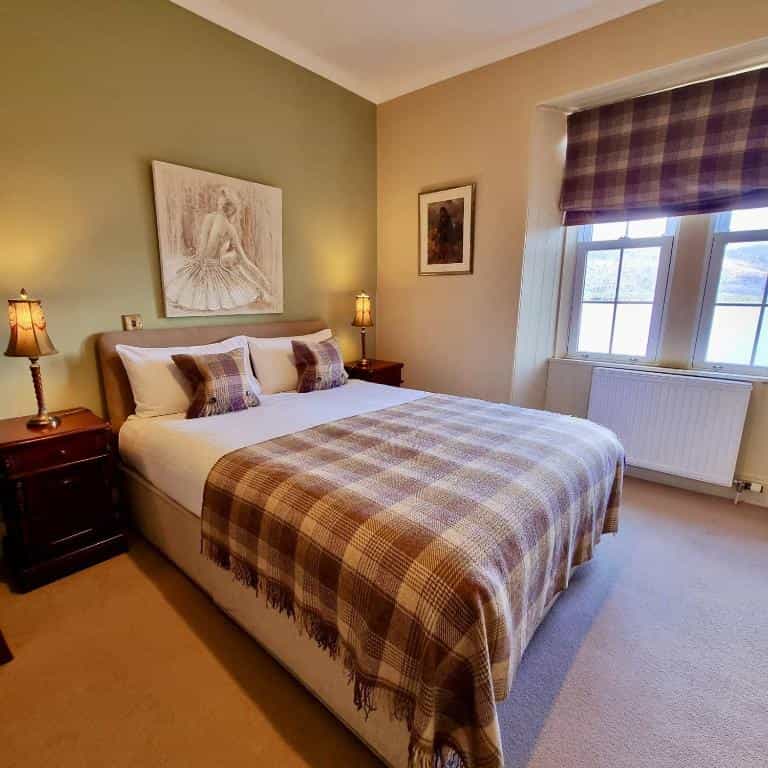 Hotel room with double bed, plaid throw, and artwork, near window in Loch Maree.