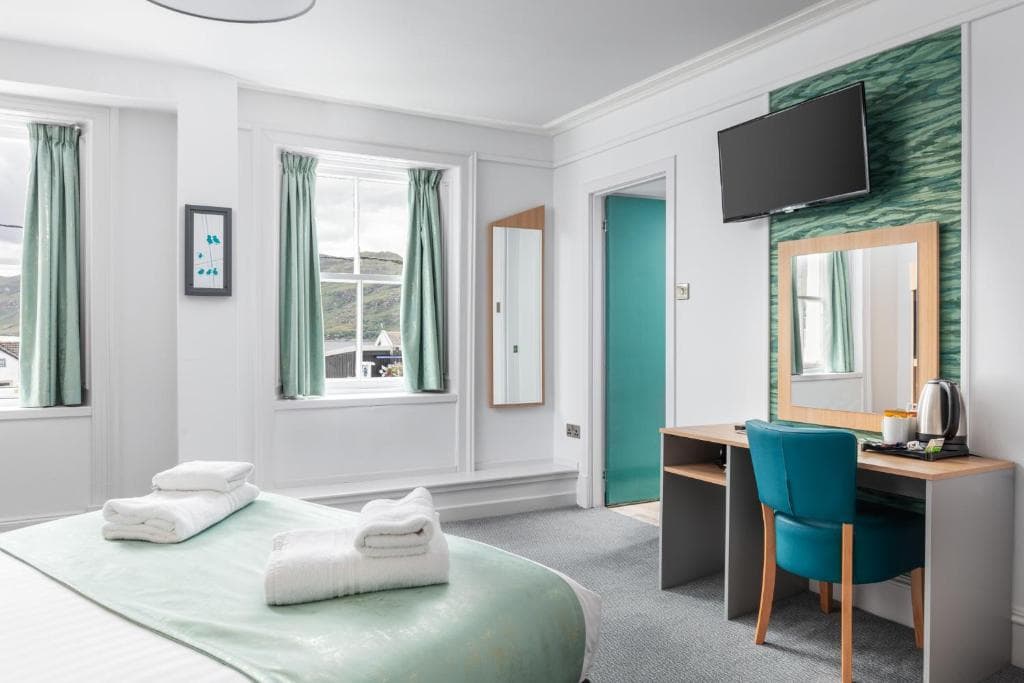 Hotel room with white walls, mint green accents, and view of green hills through windows.