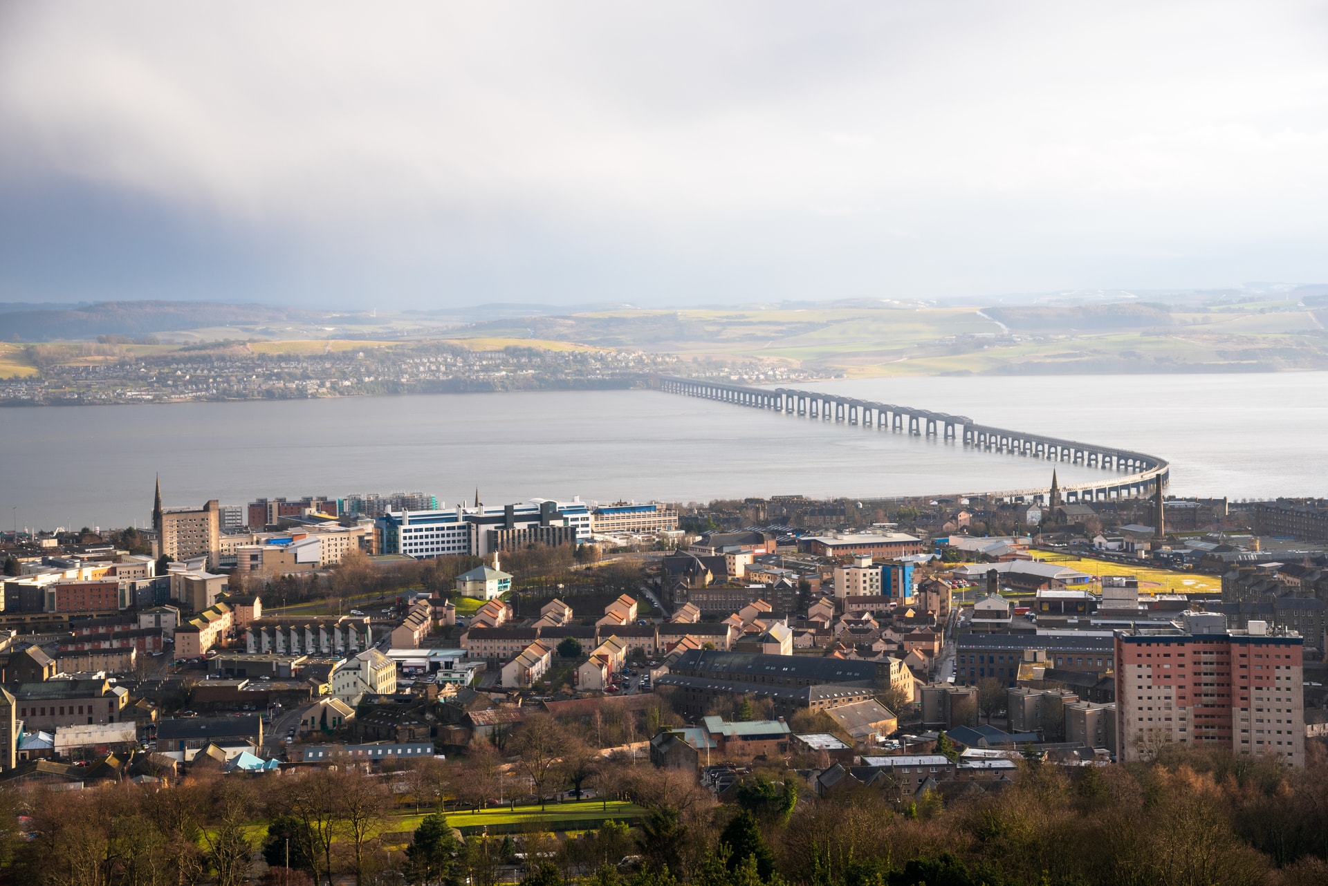 Panoramic view of Dundee city with the Tay Rail Bridge spanning the water under a bright sky.