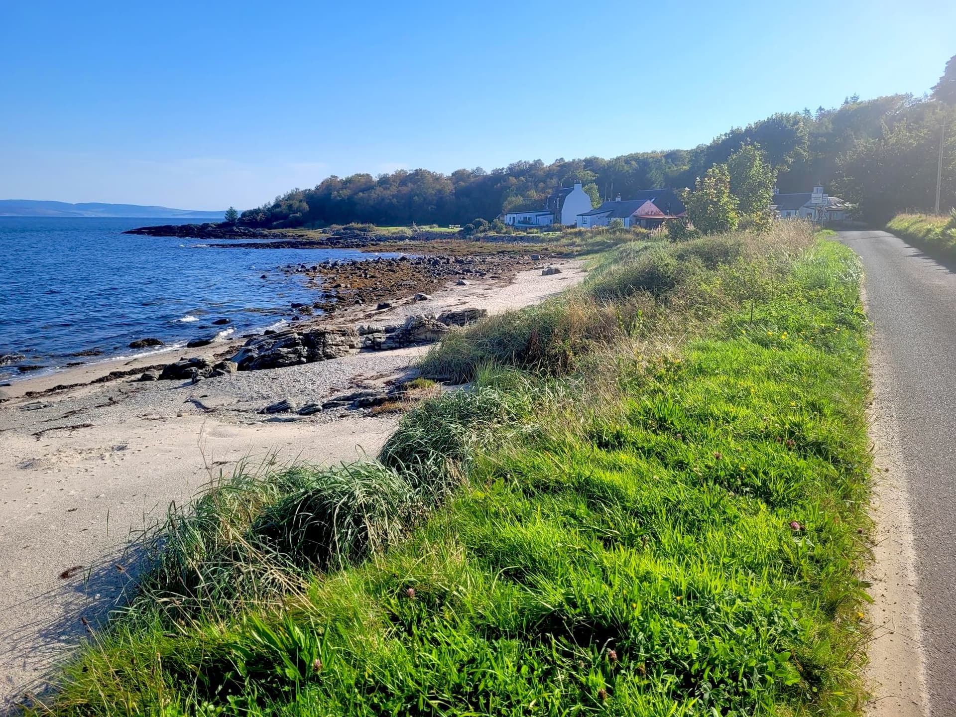 Coastal road beside rocky beach and blue sea near houses, Campbeltown to Tarbet.