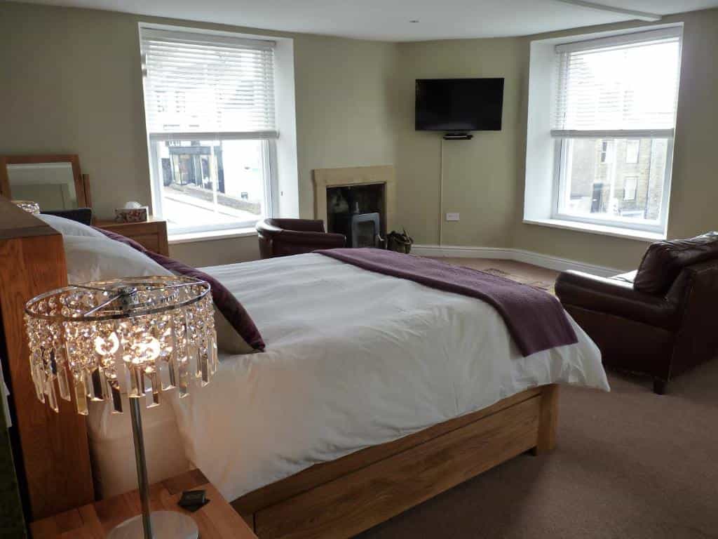 Bedroom with wooden bed, crystal lamp, leather armchair, and view through windows.