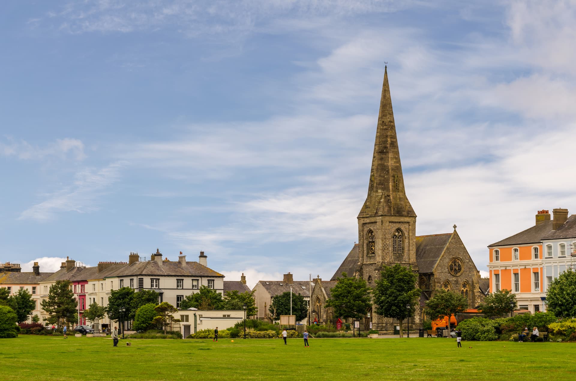 Stone church with tall spire overlooking green park with people and colorful terraced houses in Silloth.