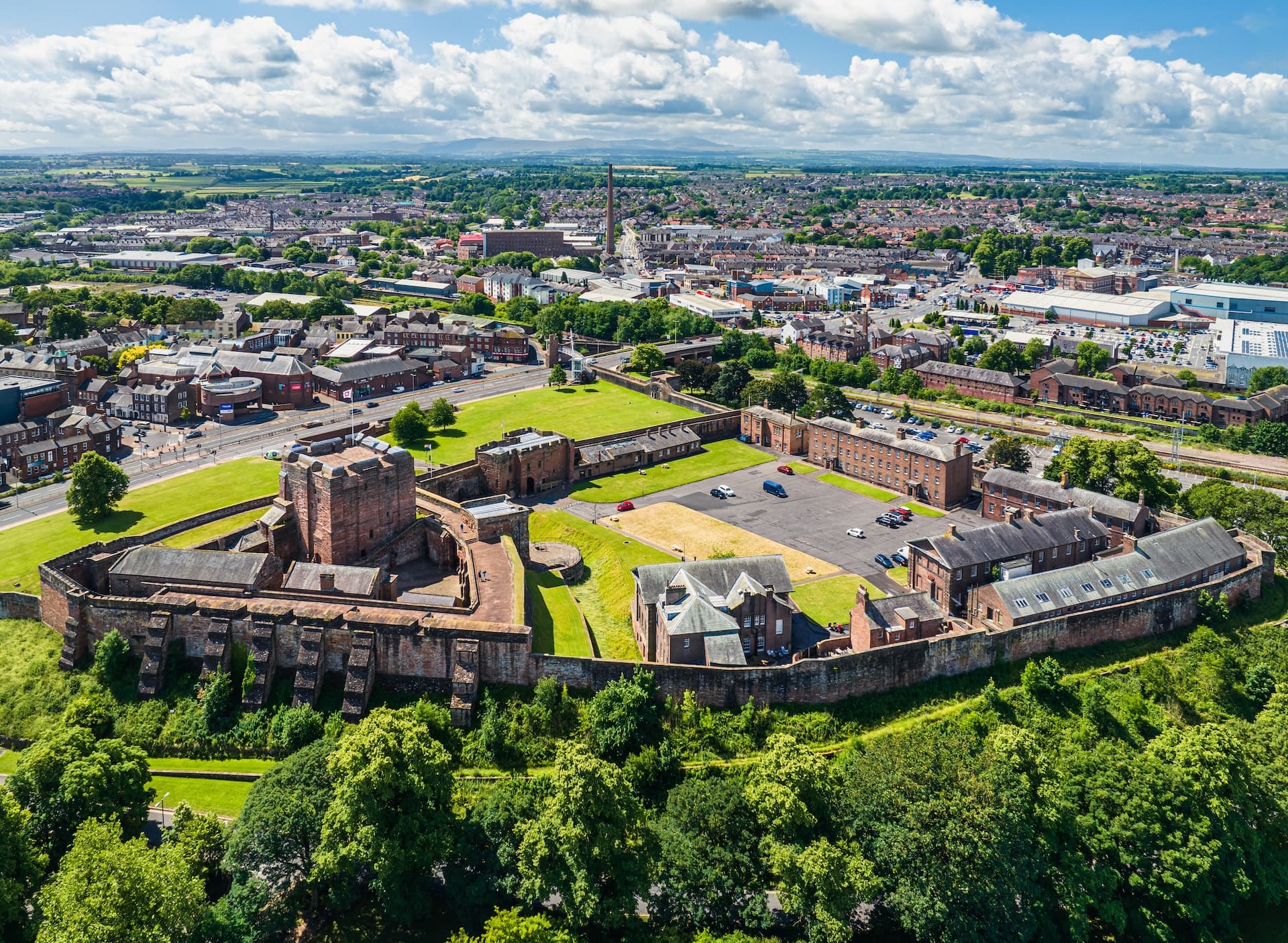 Aerial view of Carlisle Castle walls and grounds overlooking the town under a partly cloudy sky.