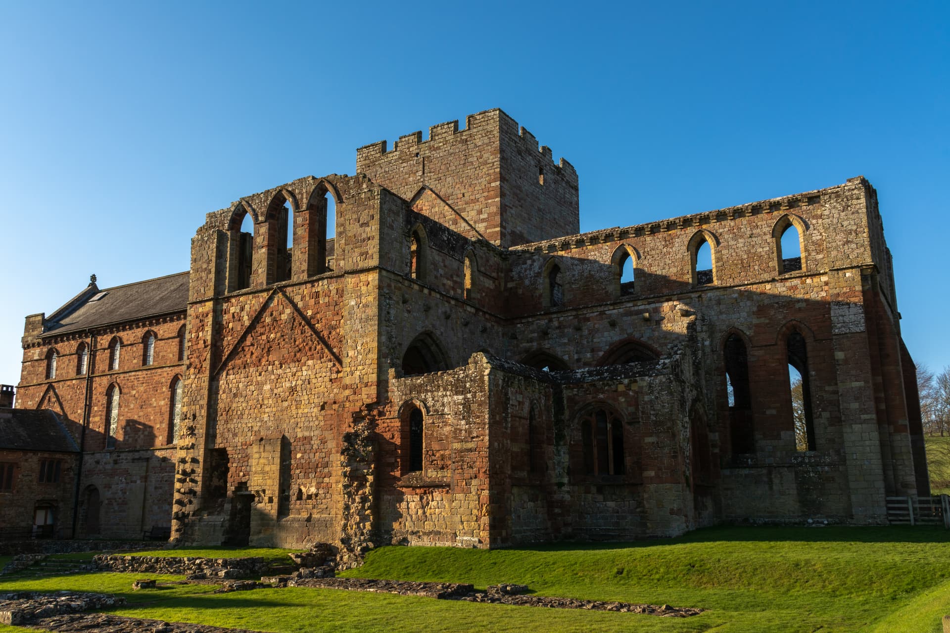 Ruins of a large stone priory building with arched windows against a clear blue sky.