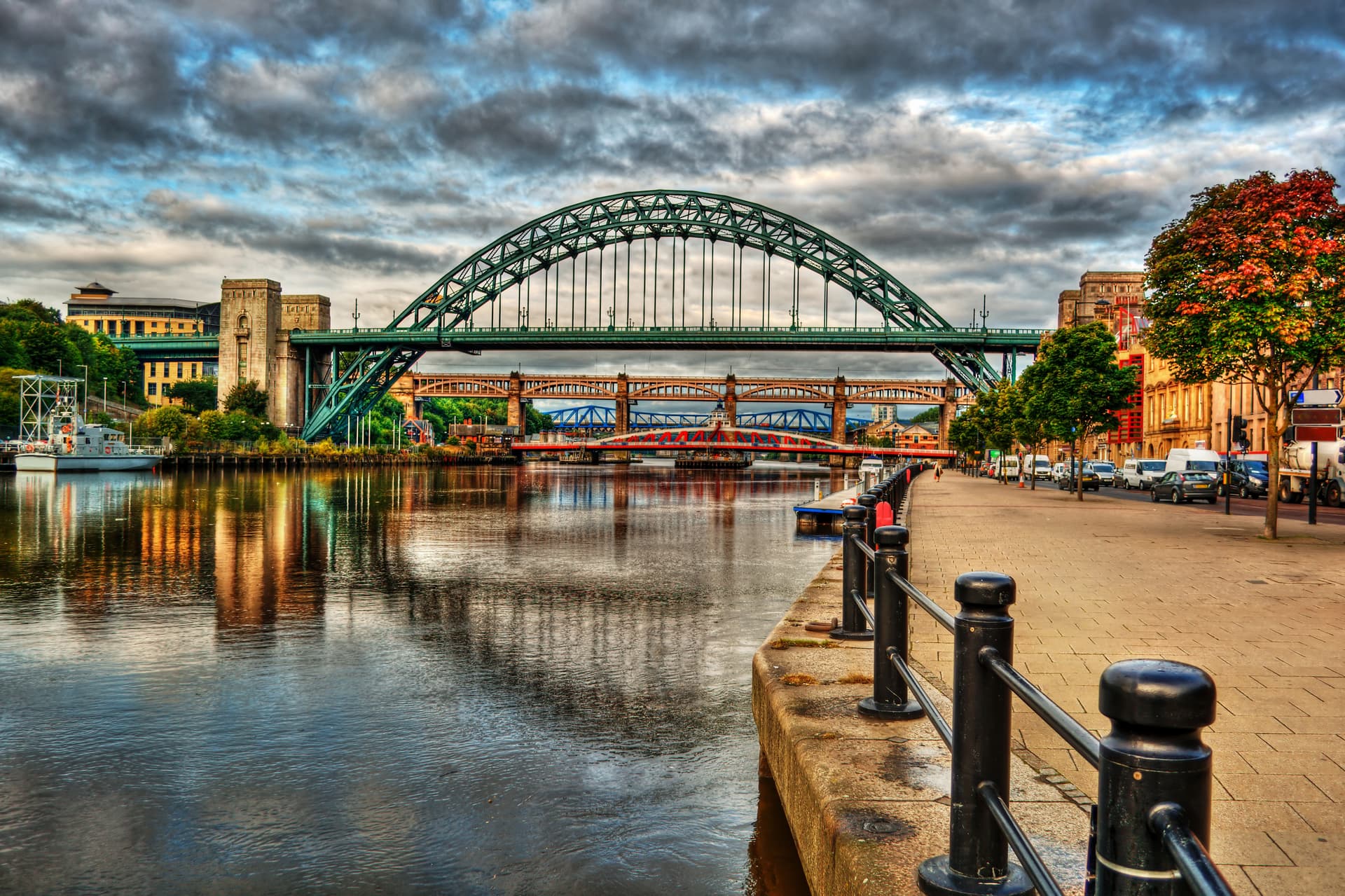 Tyne Bridge and other bridges over the river with a quayside walkway and autumn trees in Newcastle.
