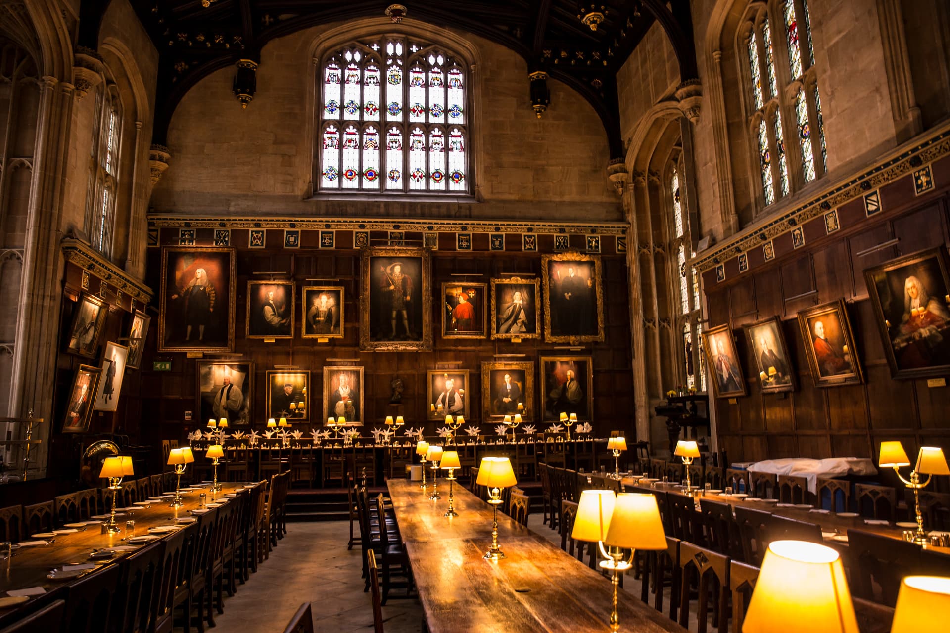 Dining hall interior at Oxford University with long wooden tables, portraits, and stained glass windows.