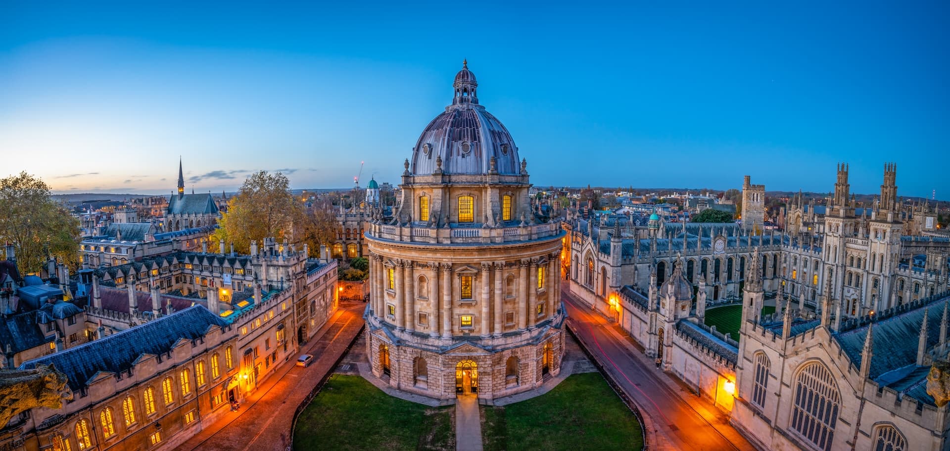 Radcliffe Camera dome and historic university buildings illuminated at dusk in Oxford.