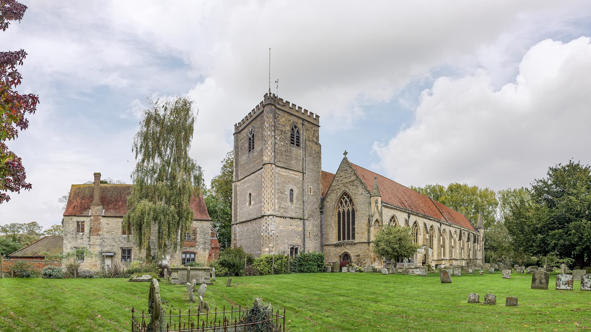 Stone church with square tower and adjacent historic house in Dorchester-on-Thames churchyard.